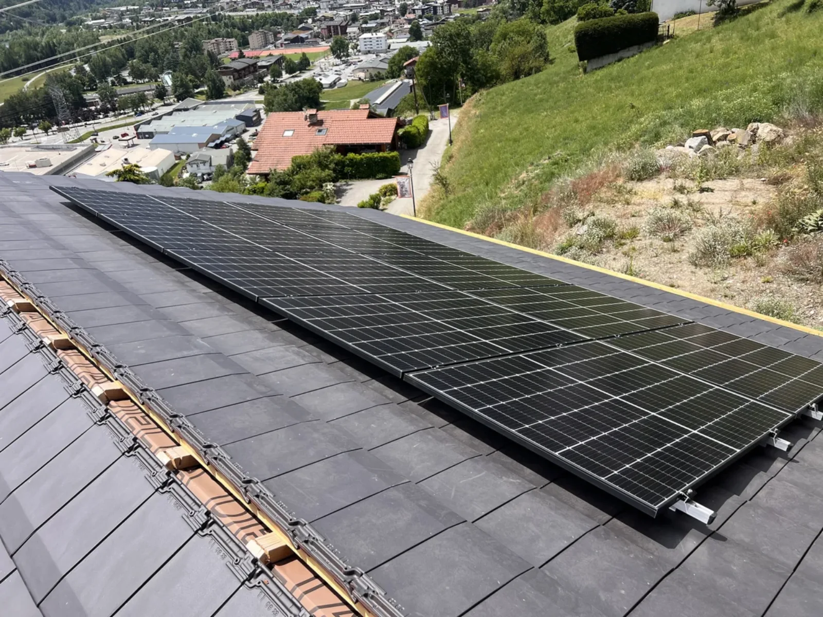 vue d'un des deux pans de toiture d'une maison particulière équipé de panneaux solaires, vue plongeante sur les habitations en-dessous