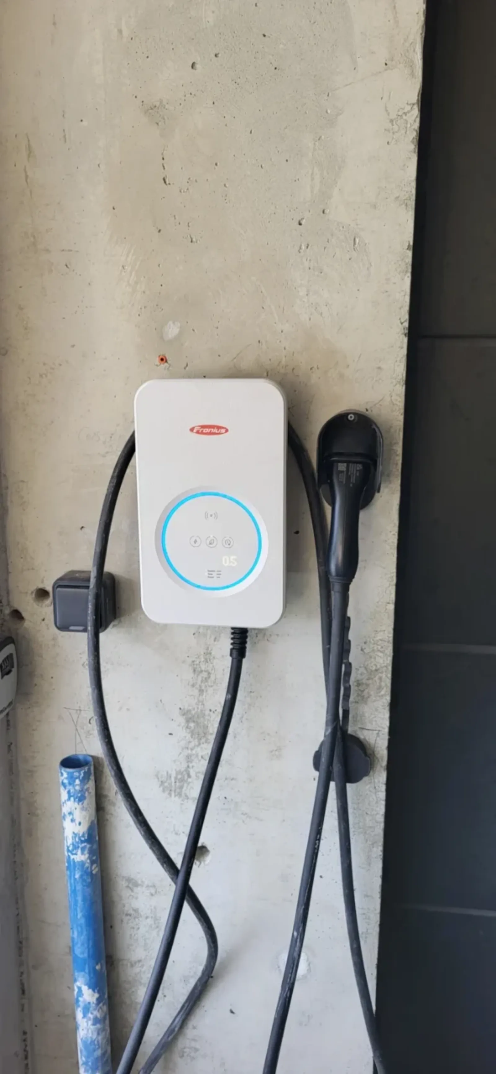 Borne de recharge 7kw FRONIUS posée sur le mur intérieur du garage d'une habitation, voyant allumé en état de fonctionnement