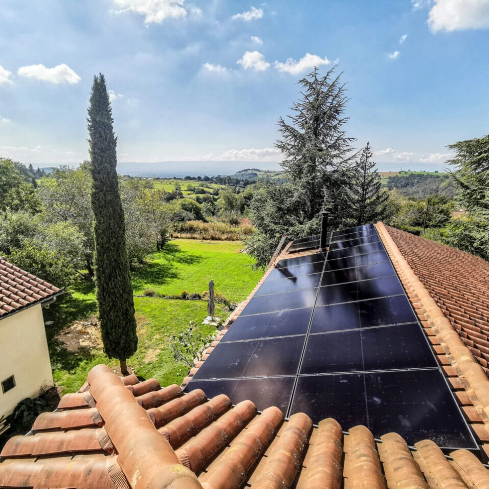 Panneaux solaires photovoltaïques sur toiture en tuiles d'une maison individuelle, journée ensoleillée, jardin verdoyant