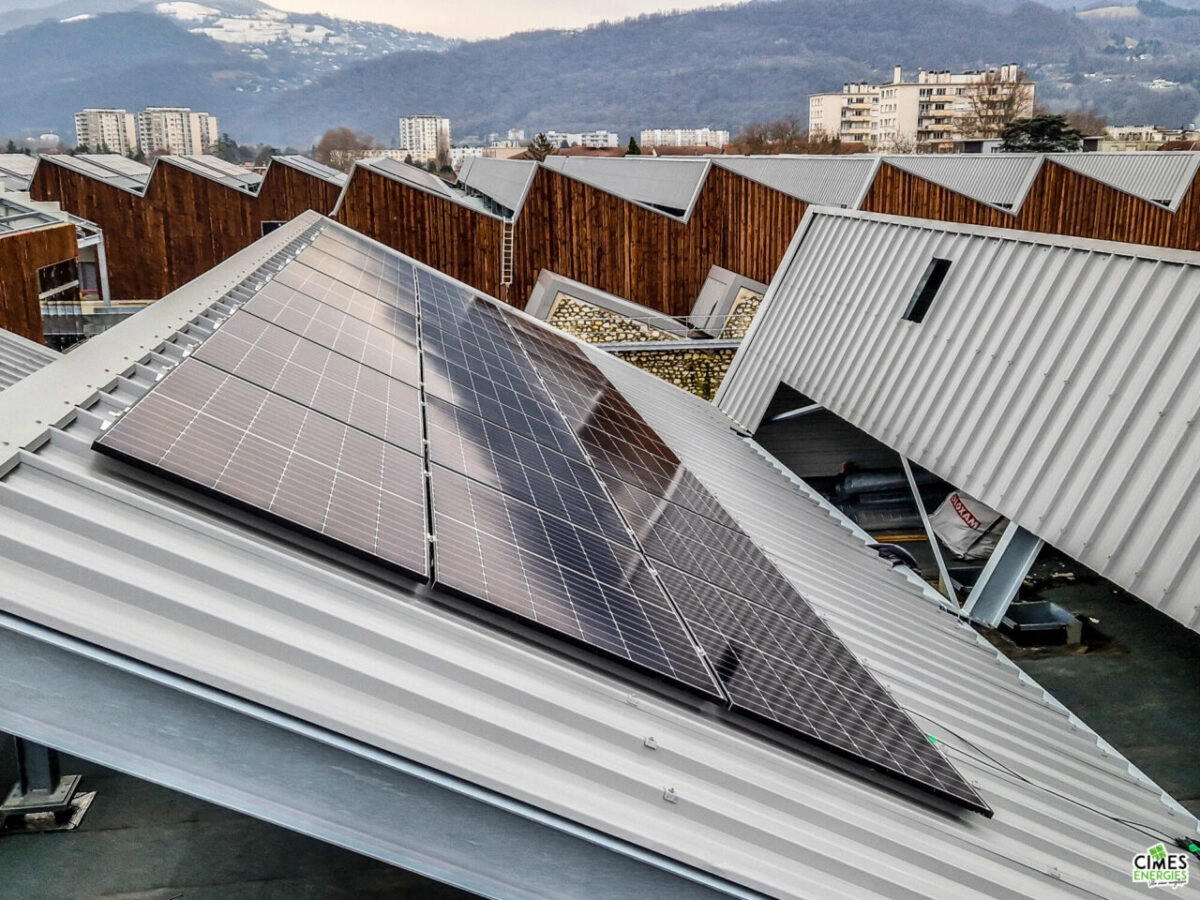 Installation solaire phtotovoltaïque sur l'un pand de toiture du centre commercial Neyrpic à Grenble, vue de côté avec montagnes en arrière-plan.